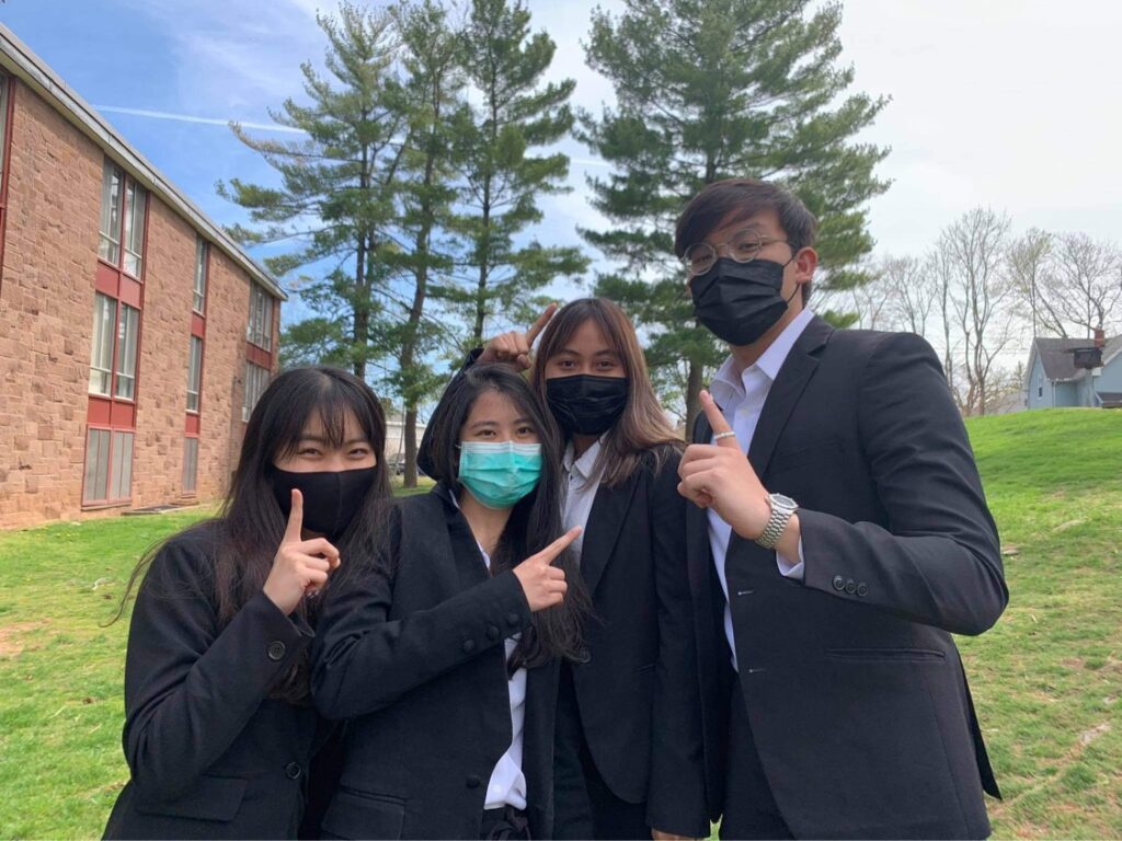 Four team members, dressed in blazers and wearing masks, show thumbs up.